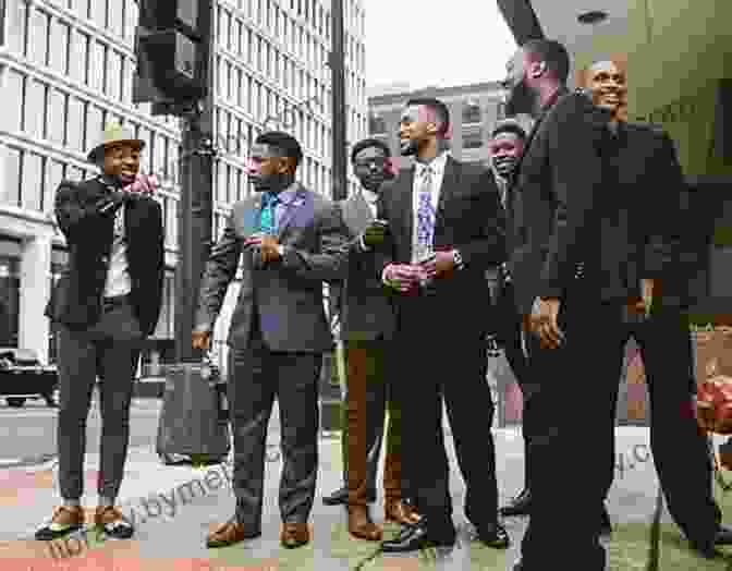 A Group Of Young Black Men Stand In A Line, Smiling. They Are Dressed In Black Suits And Ties. The Background Is A White Wall. A BLACK FIRST: The Blackness Continues